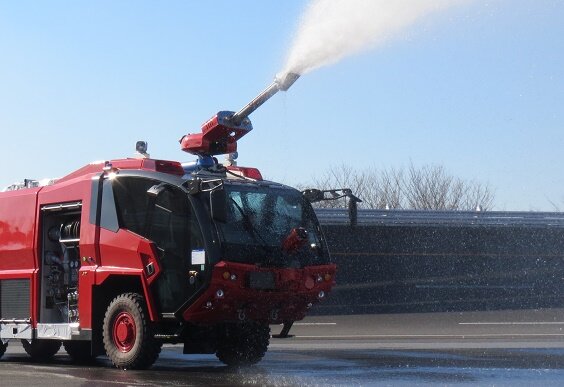 空港用化学消防車が滑走路上で放水訓練を行っている様子。高圧放水ノズルから水を噴射し、航空機火災に備えた消防対応を実施している。
