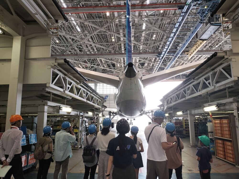 格納庫内で、航空機の構造や設備について説明を受けている見学者の様子