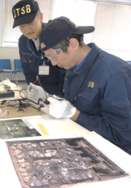 事故機部品の写真を確認しながら、室内で精密な調査作業を行う職員の様子
